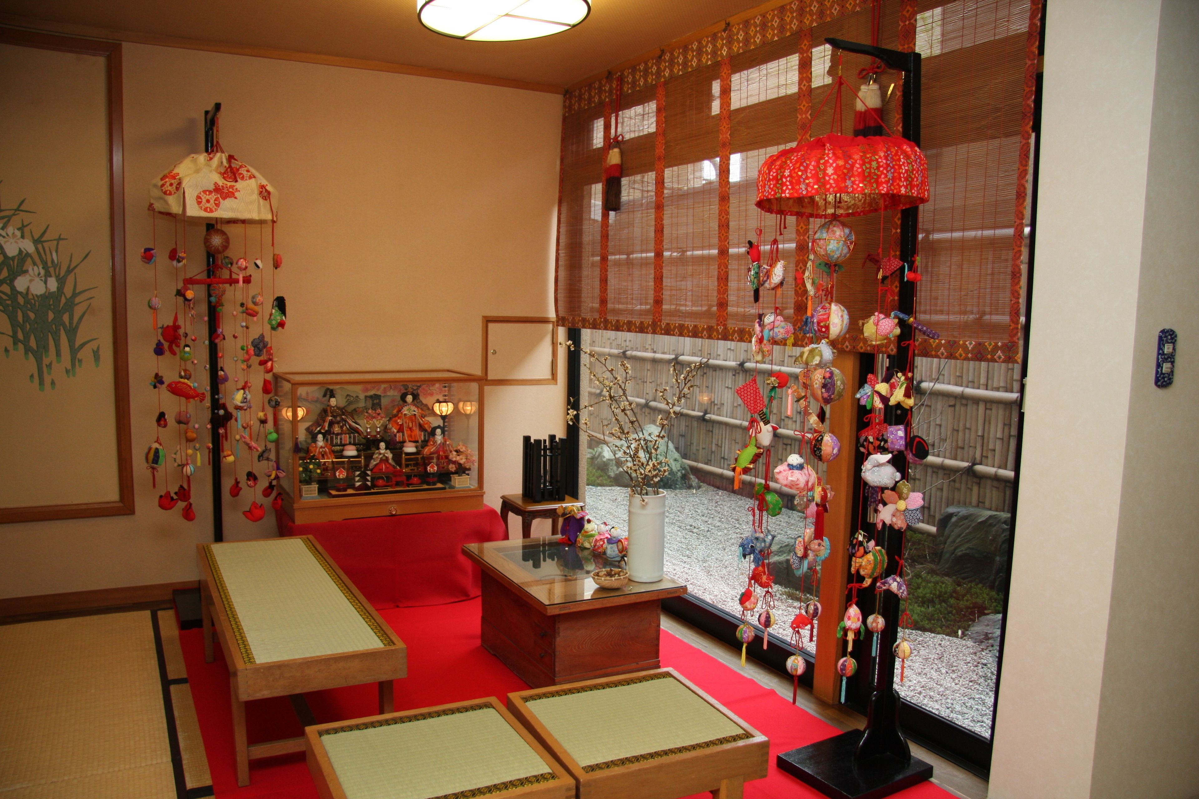 Una habitación japonesa tradicional con suelo de tatami, una mesa de madera baja, un sofá rojo y un ventanal con vistas a un jardín.