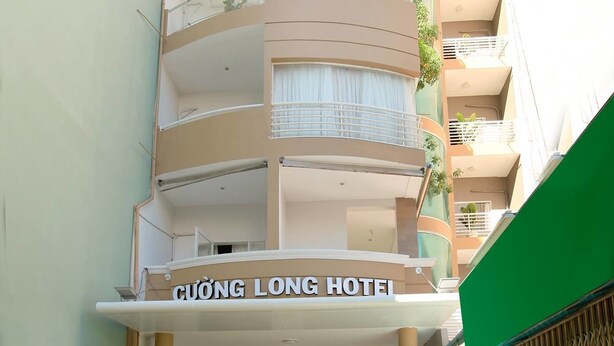 Un hotel de varios pisos con fachada curva, balcones con plantas y un letrero que dice 'CUONG LONG HOTEL'.