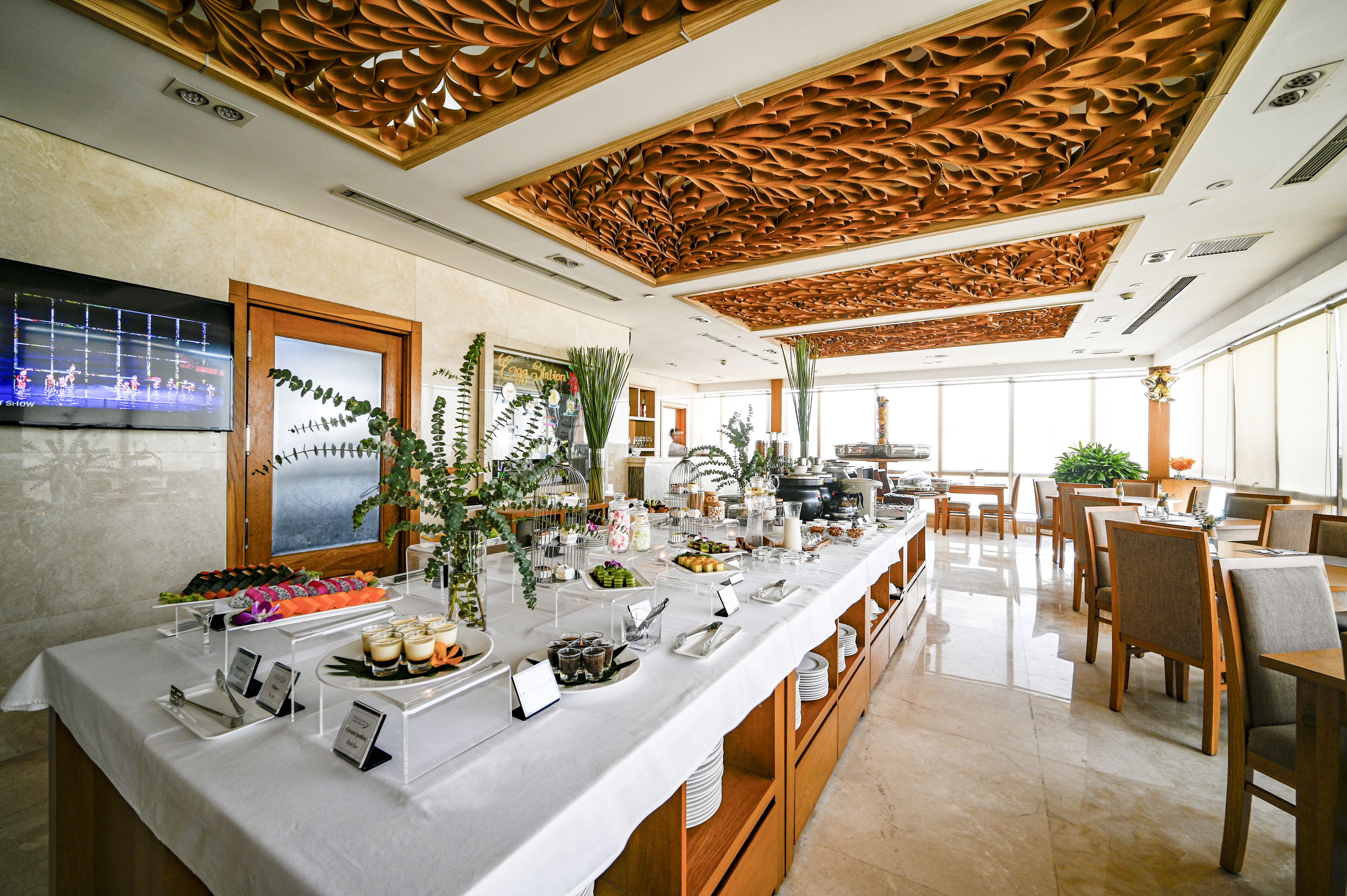 Mesa de buffet con diversos alimentos, una pantalla de televisión y un diseño de techo de madera.