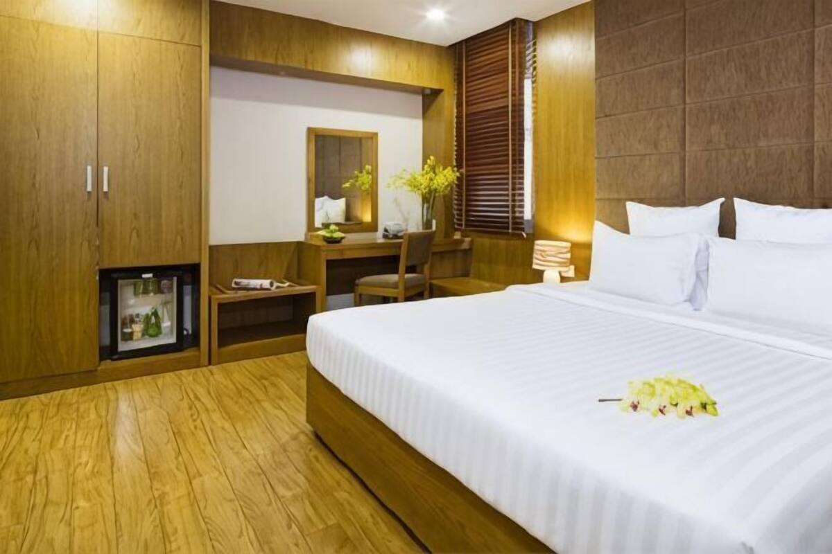 A hotel room with a bed, a desk, a chair, a small refrigerator, and a mirror.