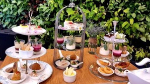 Una mesa servida con una variedad de alimentos y bebidas, que incluye un soporte escalonado para postres, una tetera y una taza de té.