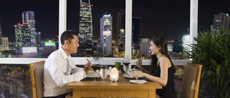 Una pareja cenando en una mesa con vistas a la ciudad, incluyendo un rascacielos característico.