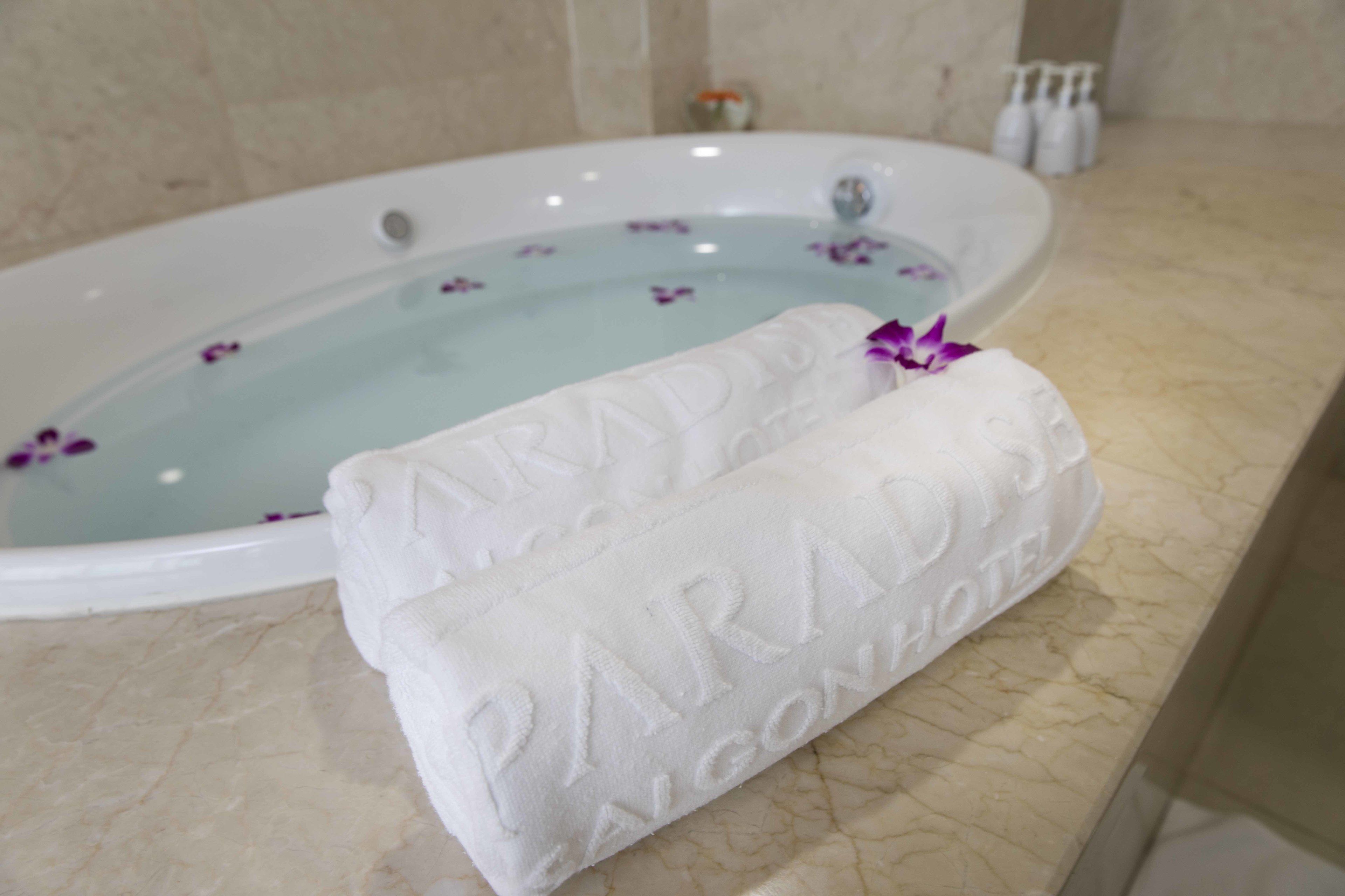Une baignoire décorée de motifs floraux et une serviette portant l’inscription « PARADISE L’AGON HOTEL ».