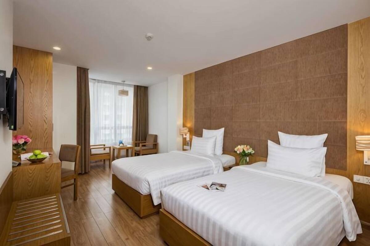 A hotel room with two beds, a desk, a chair, a TV, and a window with curtains.