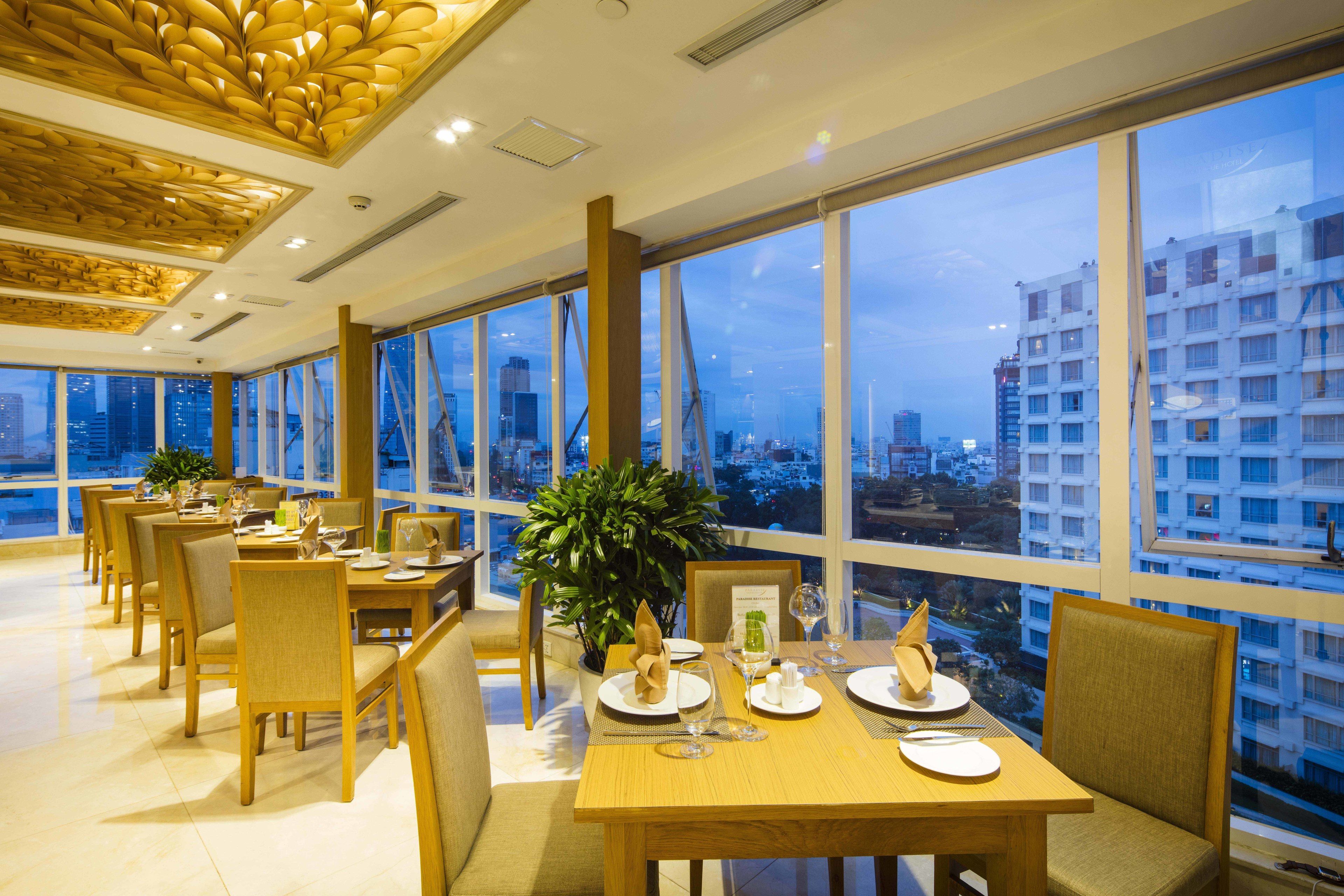 Comedor con mesas dispuestas para una comida, ventanas amplias con vista a la ciudad y un diseño de techo moderno.