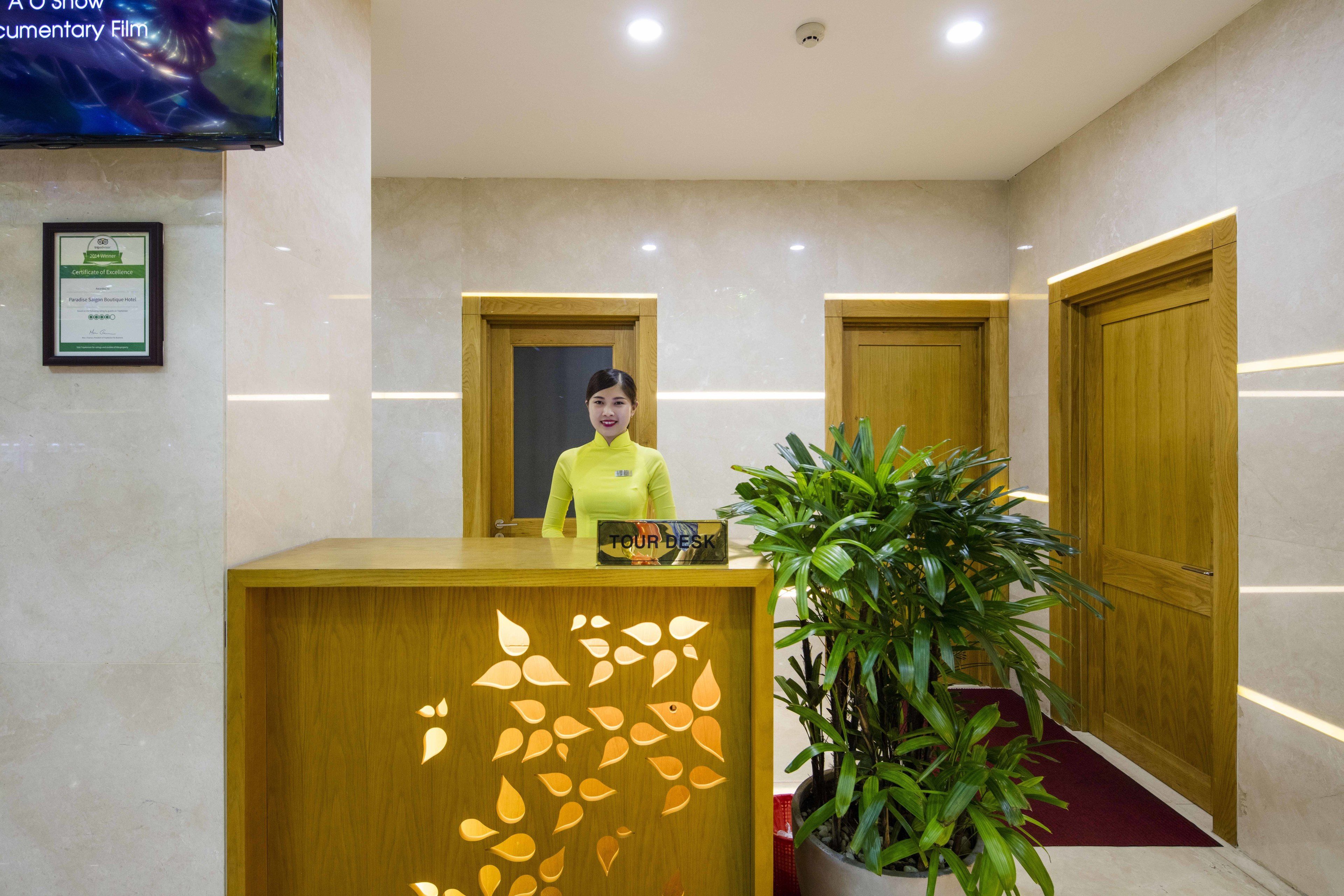 A reception desk with a wooden design, a potted plant, and wooden doors in a modern lobby.