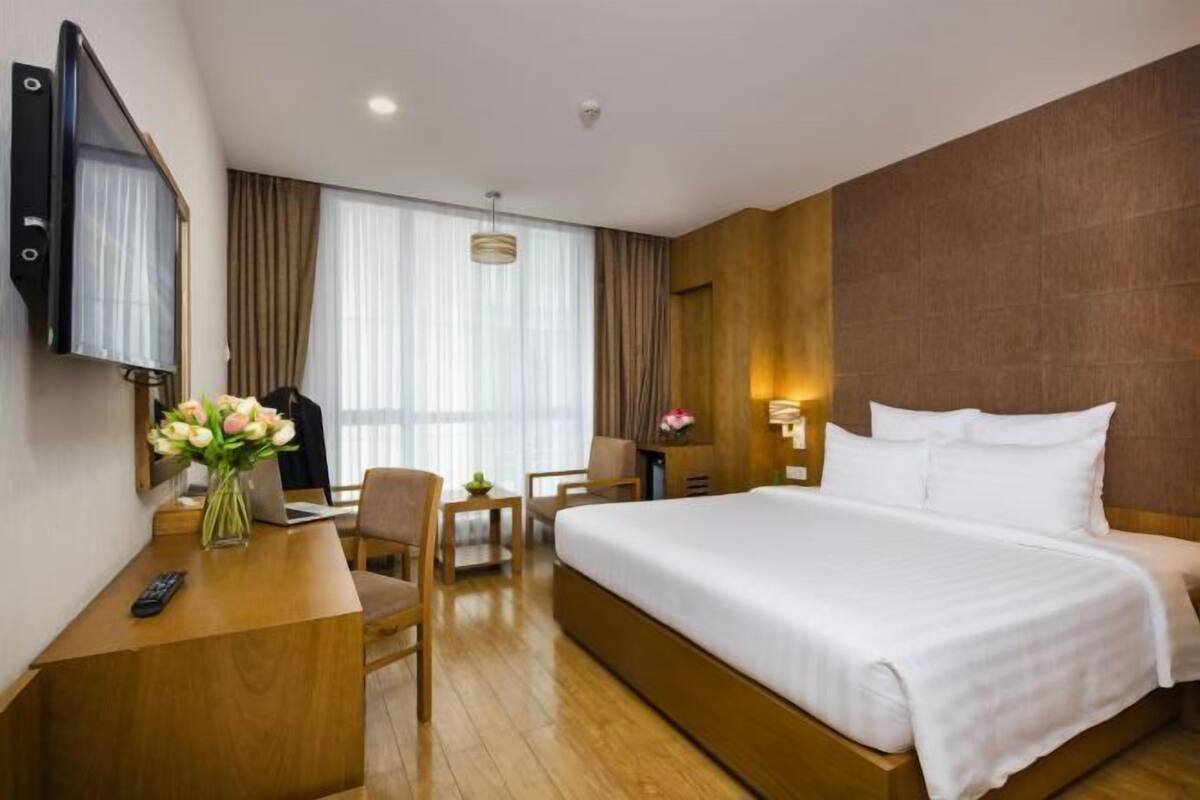 A hotel room with a bed, desk, chair, TV, and a large window with curtains.