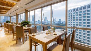 A modern dining area with large windows, wooden tables, and chairs, featuring a cityscape view. - Paradise Saigon Boutique Hotel & Spa (Ho Chi Minh City)