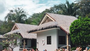 A poolside area with lounge chairs and a swimming pool, surrounded by thatched-roof buildings and lush greenery. - Phuwadee Resort & Spa (Ko Pha-ngan)