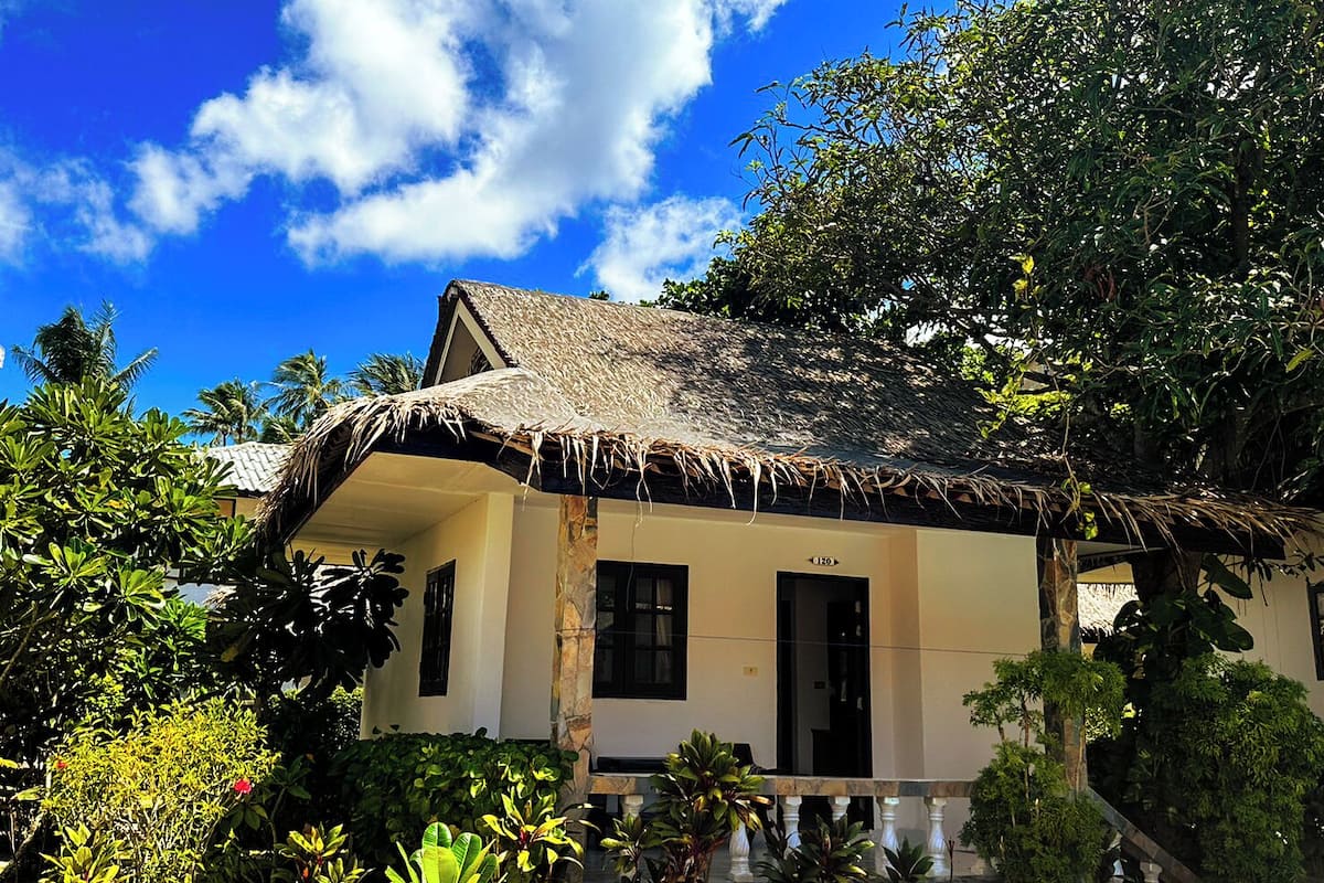 A traditional thatched-roof house with a stone base, surrounded by lush tropical vegetation.