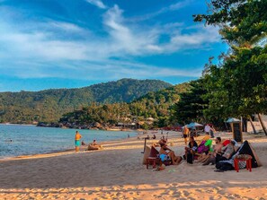 A beach with people relaxing, tents, and a view of the sea and hills. - Phuwadee Resort & Spa (Ko Pha-ngan)