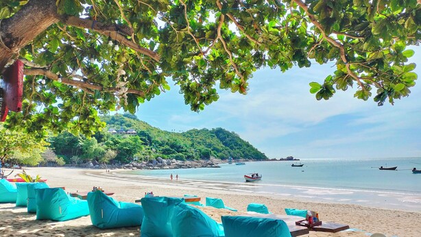 A beach with turquoise bean bag chairs, a sandy shore, and boats in the water. - Phuwadee Resort & Spa (Ko Pha-ngan)