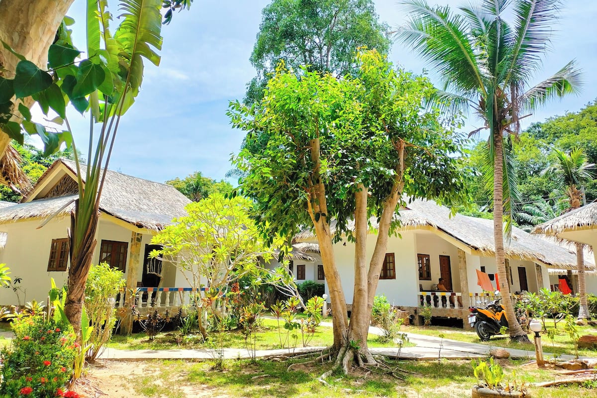 A tropical resort with thatched-roof cottages, lush greenery, and a clear sky.