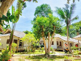 Un complexe hôtelier tropical doté de bungalows aux toits de chaume, d’une végétation luxuriante et d’un ciel dégagé.