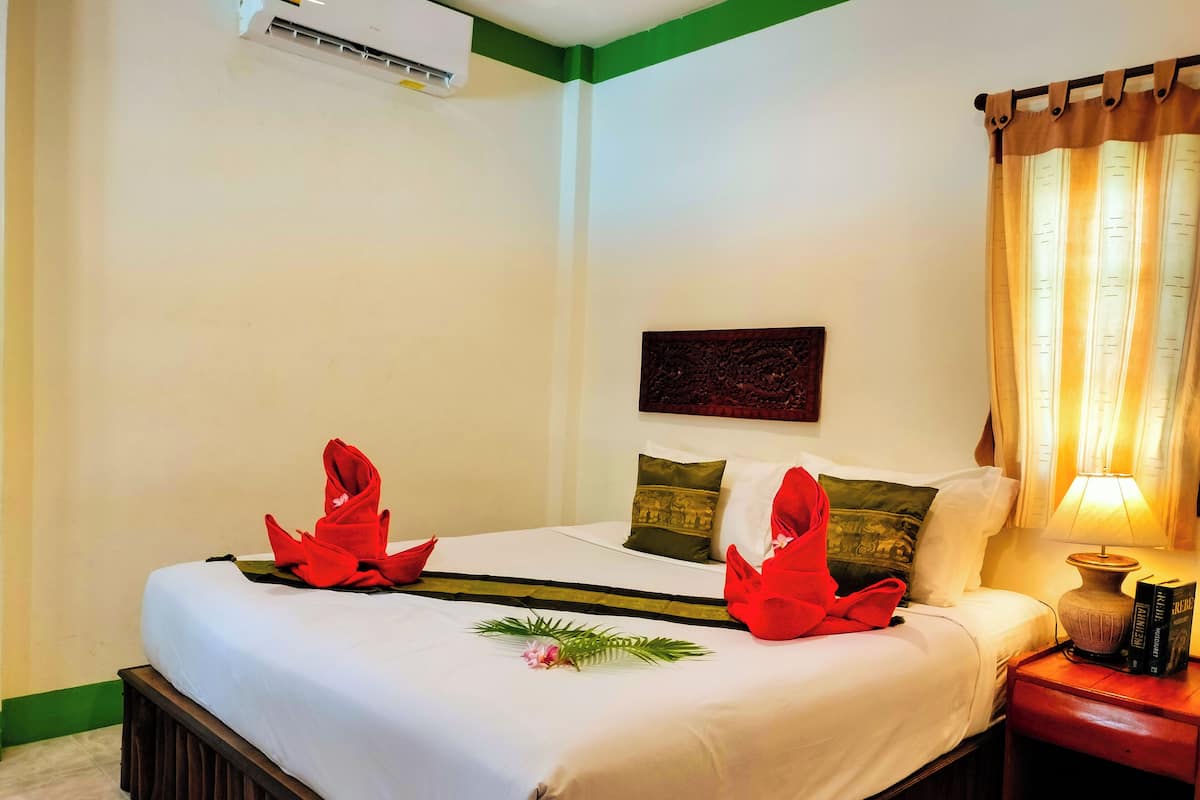 A hotel room with a neatly made bed, a bedside lamp, and a small table with books.