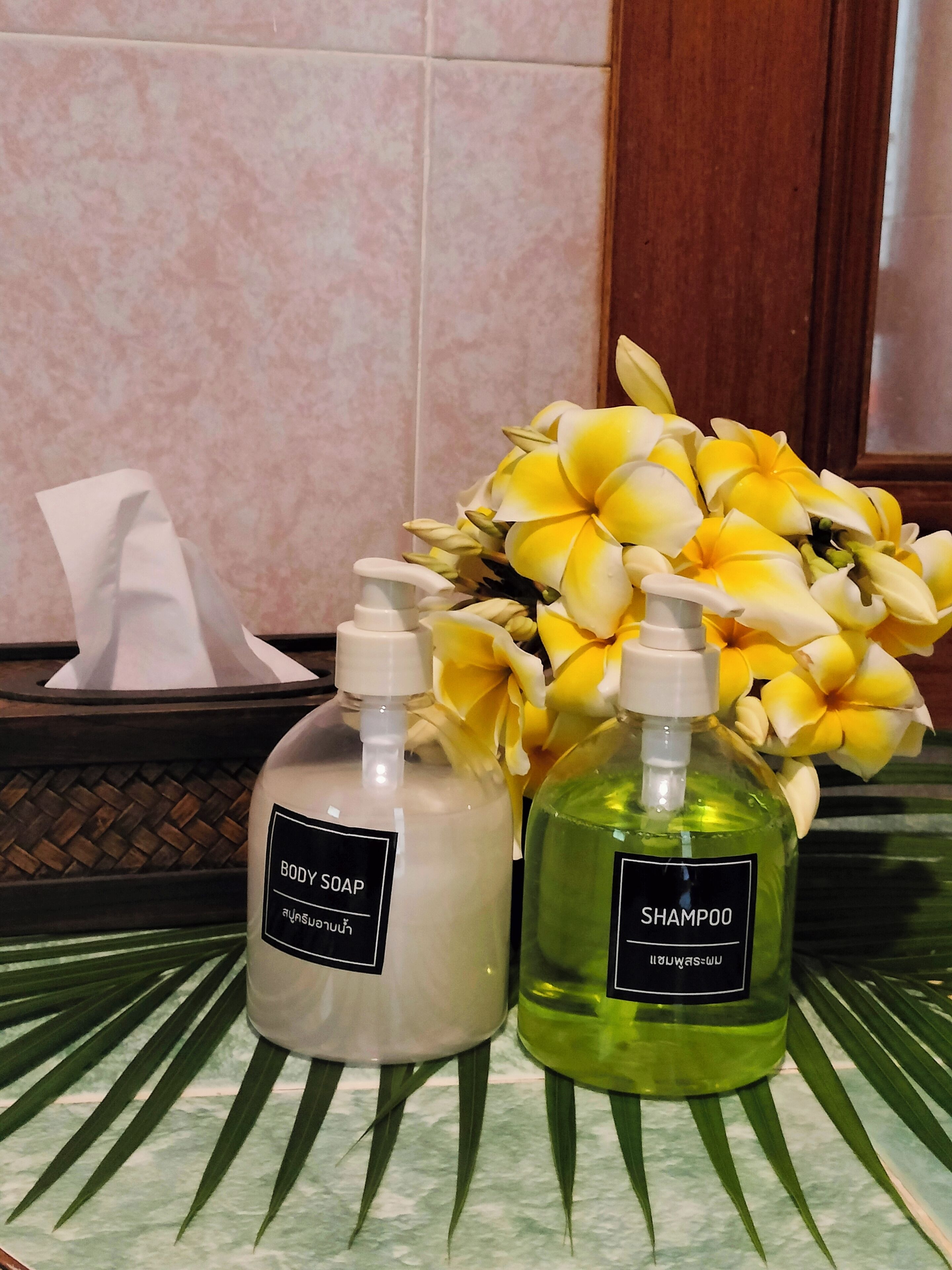 Casa de banho com bancada de mármore, duas embalagens de sabonete e shampoo, lenços de papel e um buquê de flores amarelas.