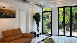 A modern interior with a sofa, a potted plant, and a large window offering a view of greenery. - White Lodge (Langkawi)