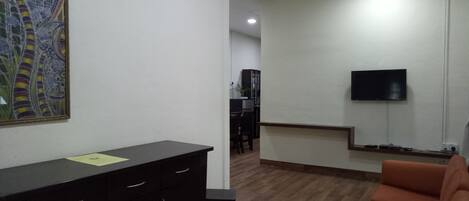 A living room with a sofa, a desk with drawers, a ceiling fan, a TV mounted on the wall, and a patterned rug on the floor.