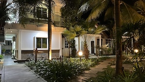 A modern building with a pathway leading to a seating area, surrounded by lush greenery and palm trees. - White Lodge (Langkawi)