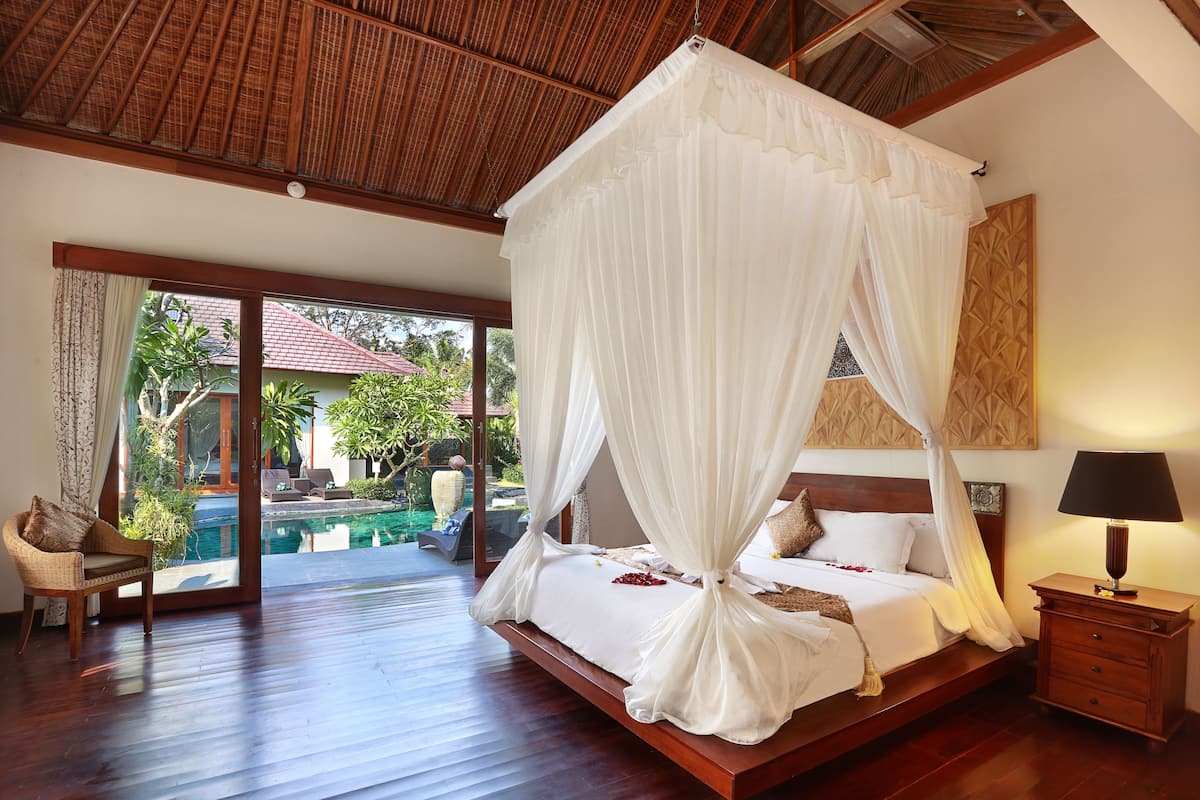 A spacious bedroom with a large bed, a nightstand, and a view of a swimming pool and garden.