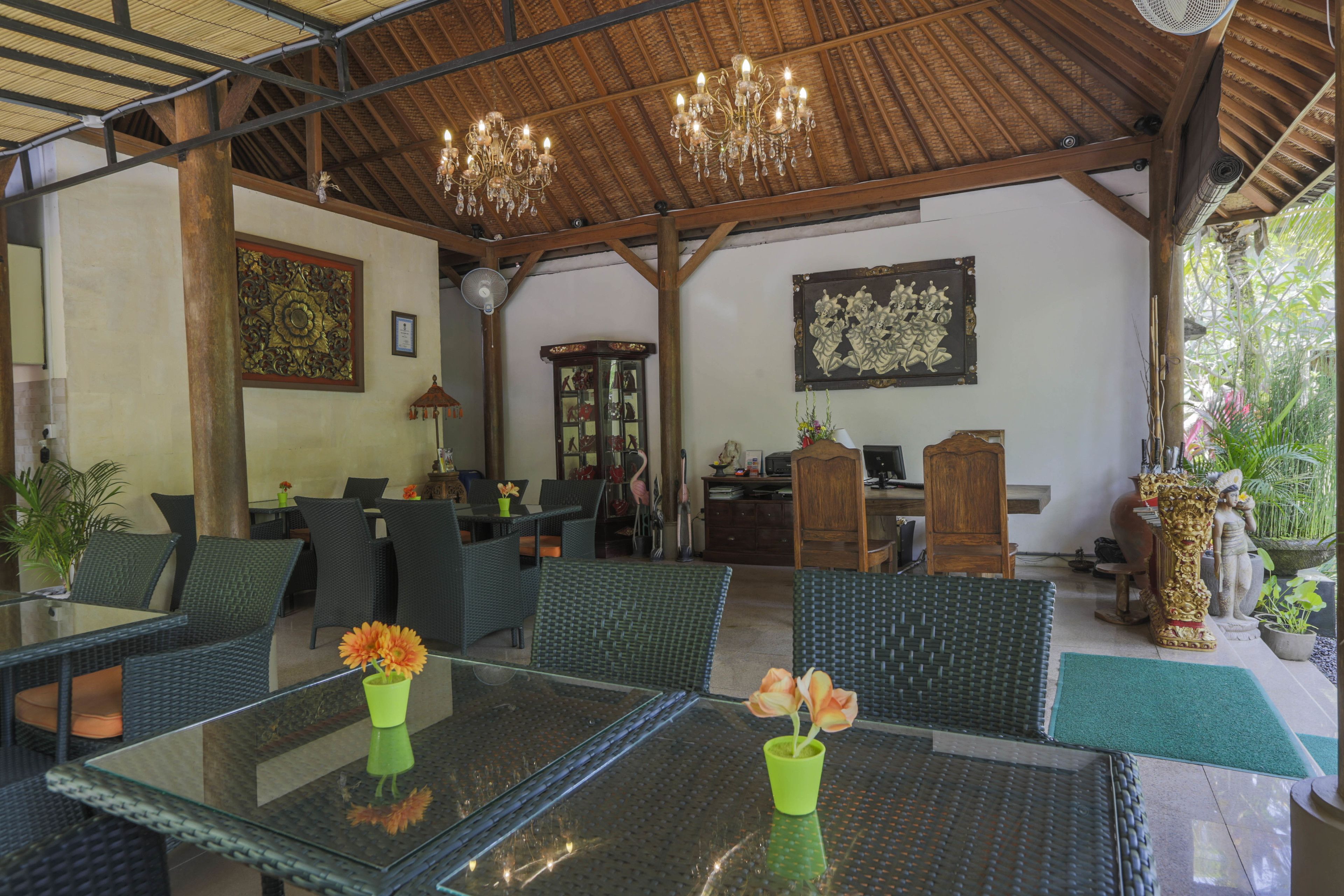 A covered outdoor seating area with wicker furniture, glass tables, and potted plants.
