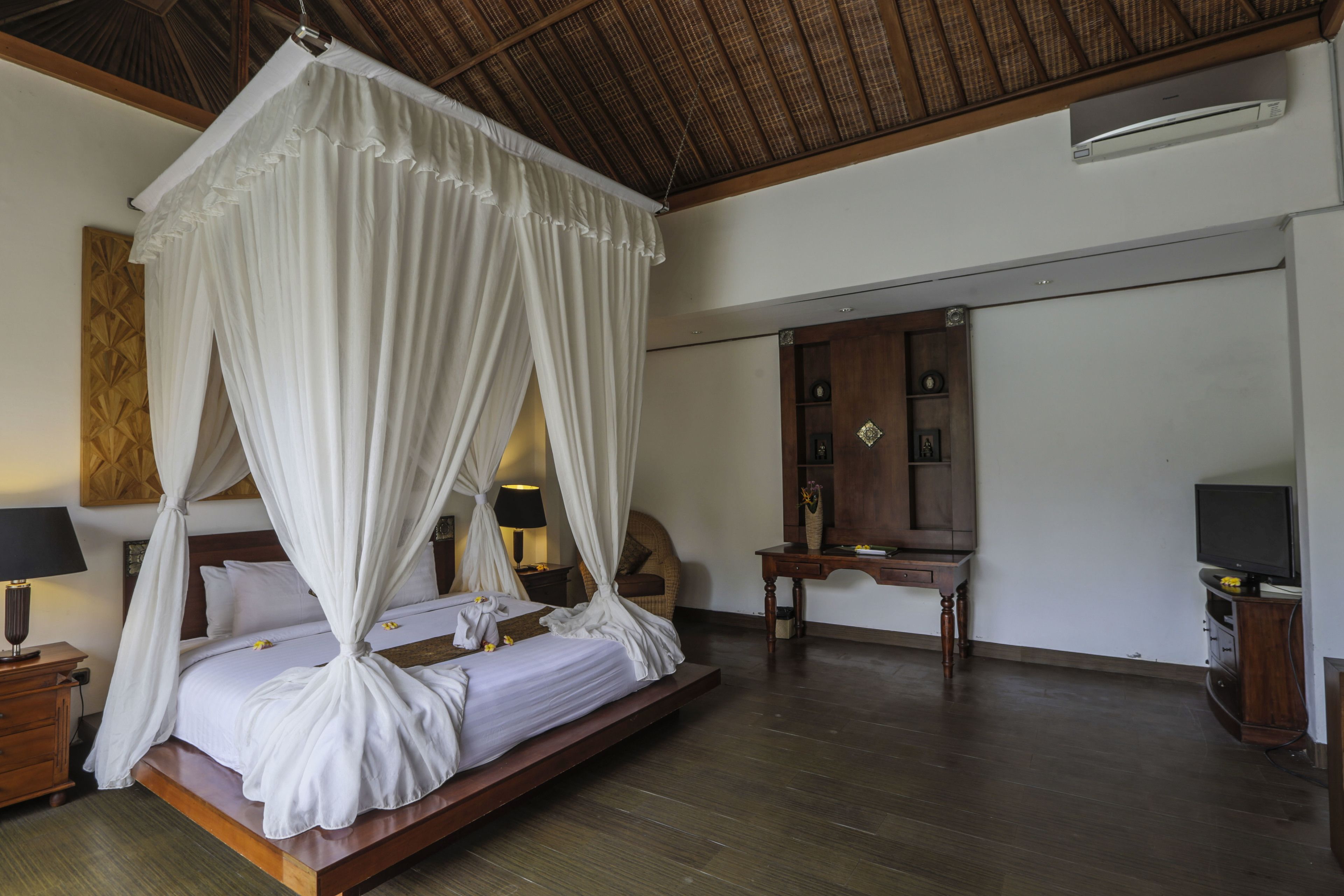 A spacious bedroom with a large bed, a wooden nightstand, a bedside table, a mirror, and a television.