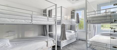 A dormitory room with bunk beds, a window with curtains, and an air conditioning unit on the ceiling.