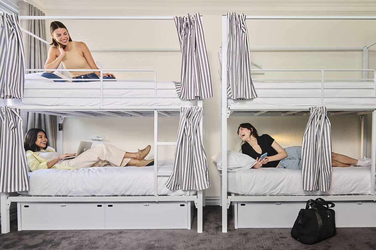 A bunk bed room with three levels, each with a white mattress and striped curtains.