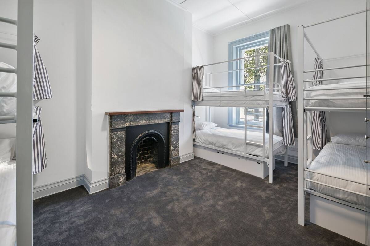 A room with bunk beds, a fireplace, and a window with curtains.