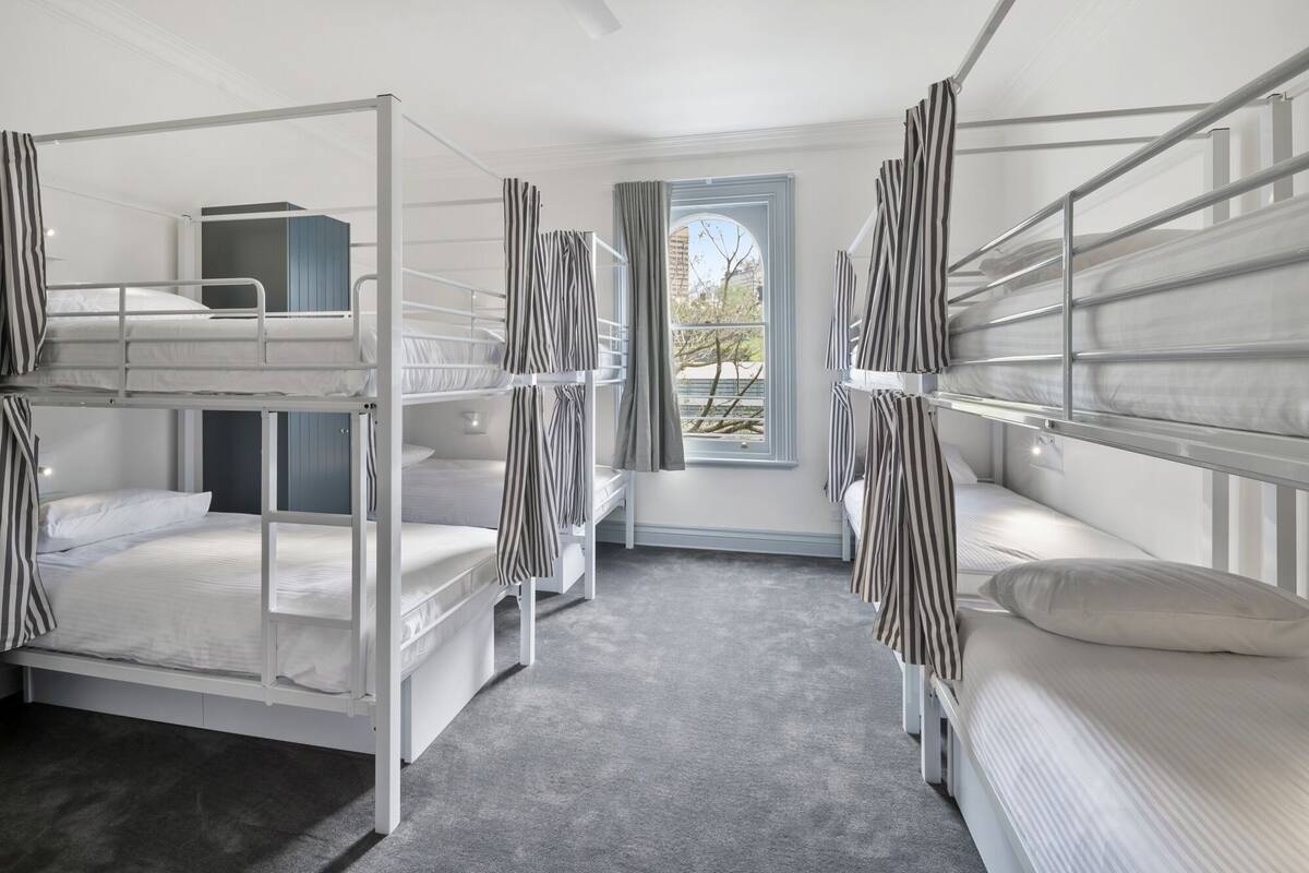 A dormitory room with bunk beds, a window with a view, and a small desk.