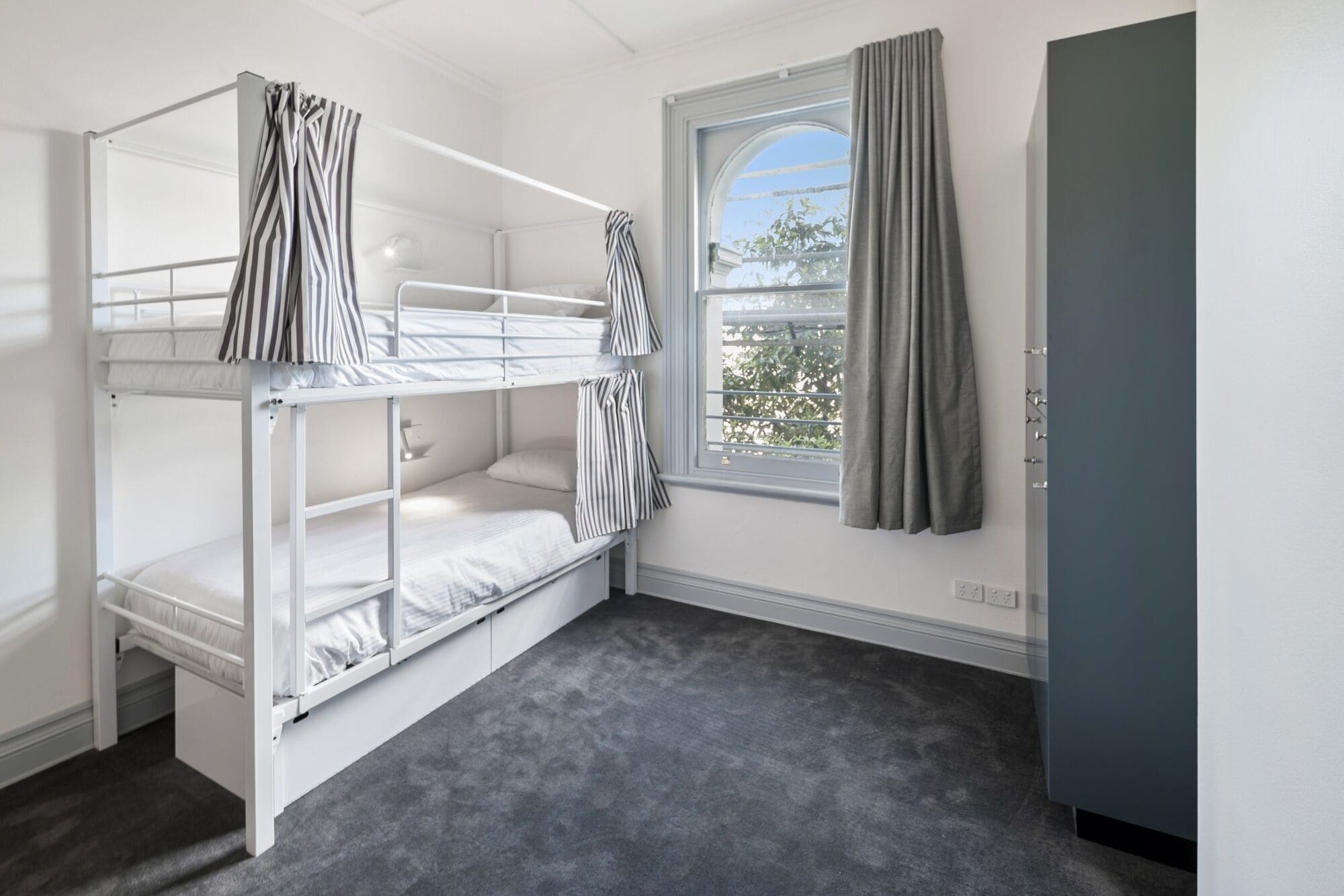 A bunk room with a window, grey curtains, and a grey wardrobe.