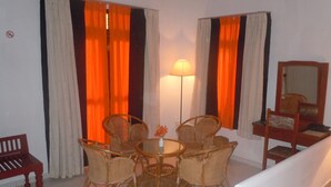 Ein Zimmer mit einem runden Tisch, vier Korbstühlen, einer Holzbank, einer Stehlampe und einem Spiegel auf einem hölzernen Podest.