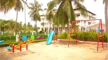 Children can play on slides and swings surrounded by lush greenery and palm trees.