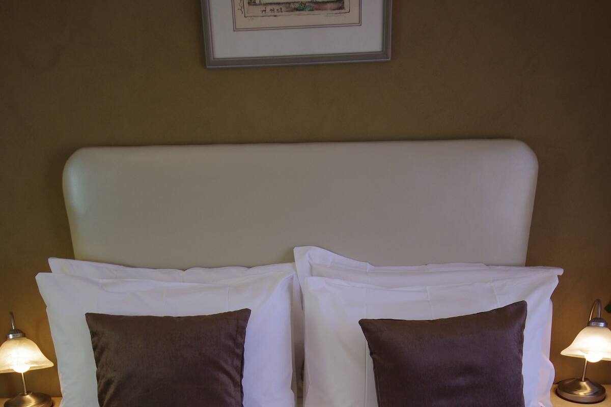 A neatly made bed with white linens and two brown pillows, flanked by two bedside lamps on matching nightstands.