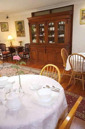 A dining area with a table set for four, a wooden cabinet, and a dining table with chairs. - Astoria Retreat B&B (Alexander Heights)