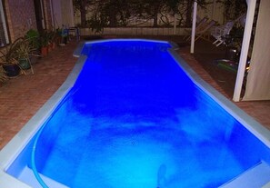 A rectangular swimming pool with a blue tint, surrounded by potted plants and outdoor furniture. - Astoria Retreat B&B (Alexander Heights)