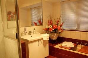 A bathroom with a white sink, a mirror, a vase of flowers, and a bathtub. - Astoria Retreat B&B (Alexander Heights)