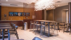 Un restaurant moderne avec des tables hautes et des chaises en métal, un luminaire décoratif et une cloison en bois ornée de tableaux encadrés.