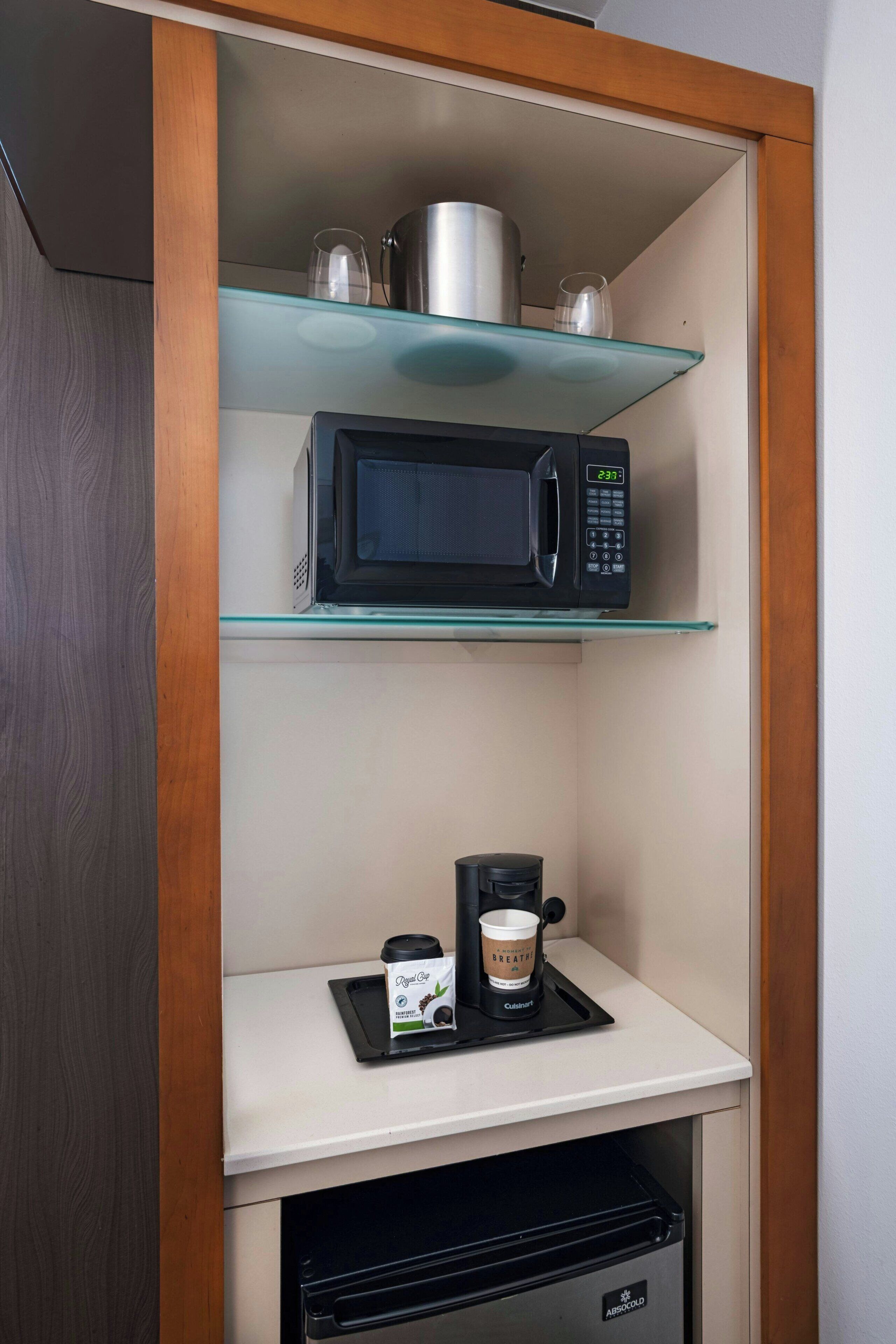 Een kitchenette met een magnetron, een koffiezetapparaat en een glazen plank.