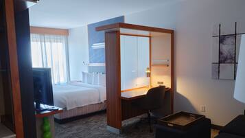 Ein Hotelzimmer mit Bett, Schreibtisch, Stuhl, kleinem Tisch und Spiegel.