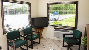 A room with two large windows, a flat-screen TV, and three green chairs.