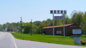 A motel sign with 'Motel' and 'Green Valley' written on it, a building with a brown roof, and a road in the foreground.