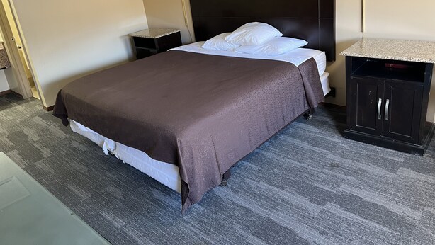 A hotel room with a bed, a nightstand, a lamp, and a cabinet.