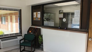 Un área de recepción con ventanal, una silla, unidad de aire acondicionado y un tablón de anuncios.