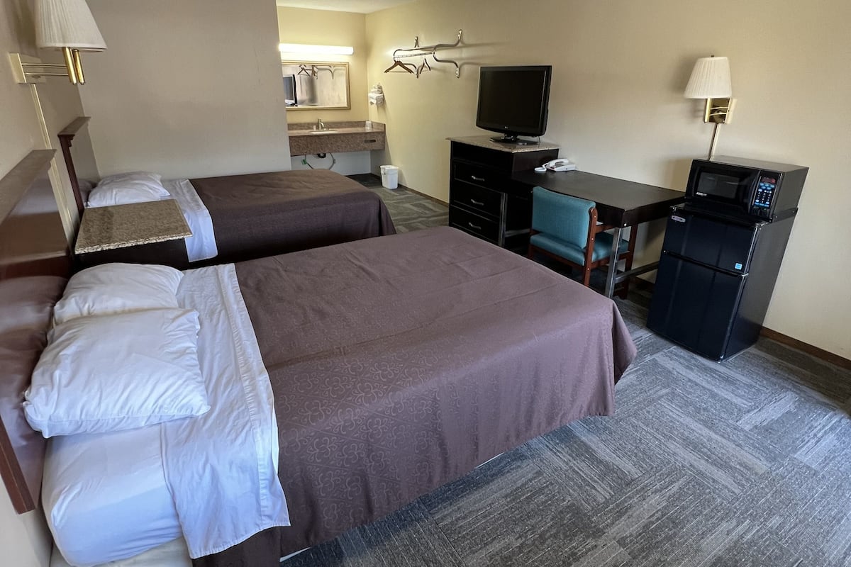 Una habitación de hotel con dos camas, un escritorio con computadora, televisor y microondas.