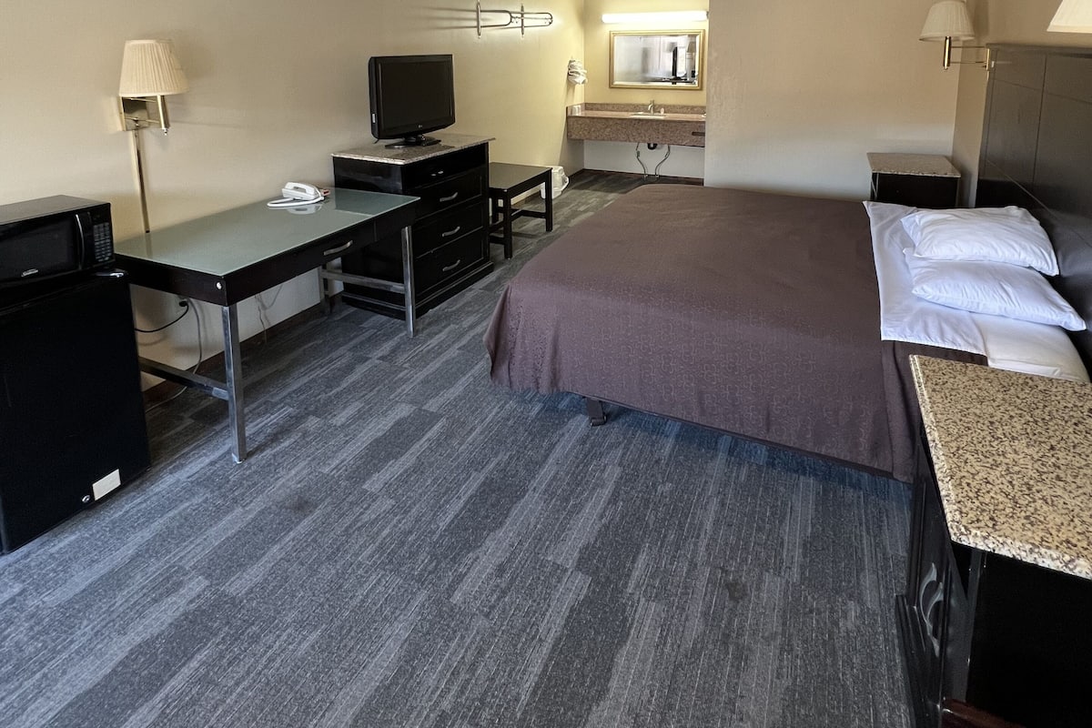 Habitación de hotel con cama, escritorio, televisión y un baño a la vista.