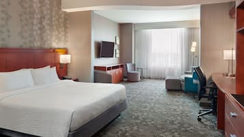 Quarto de hotel com uma cama grande, uma escrivaninha, uma cadeira e uma televisão na parede.