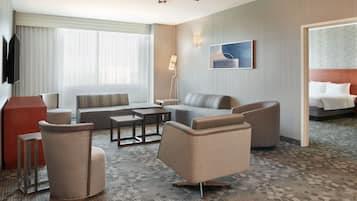 Quarto de hotel com sofá, poltronas, mesa de centro, televisão, ventoinha no teto e cama.