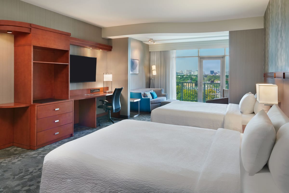 A hotel room with two beds, a desk, a TV, and a view of the city.