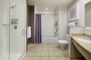 A modern bathroom with a glass shower enclosure, a bathtub, a toilet, and a granite countertop sink.